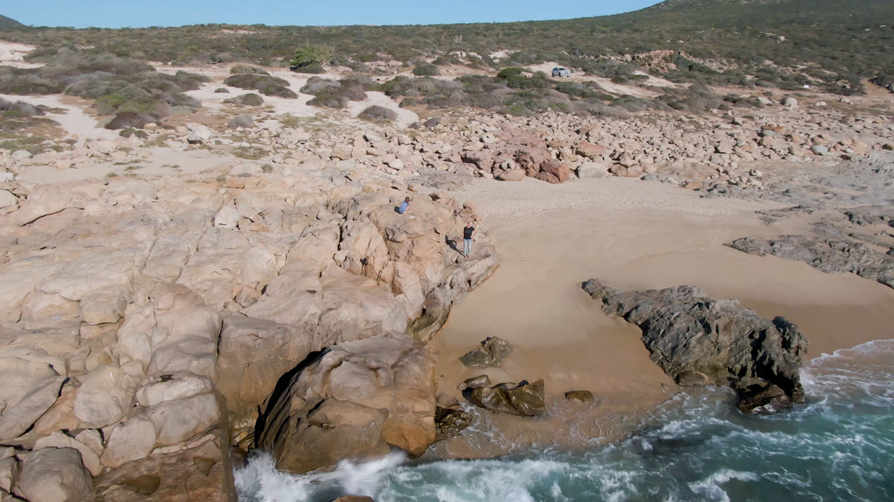 Aerial shoreline view with dark rocks and whitewater near the beach.