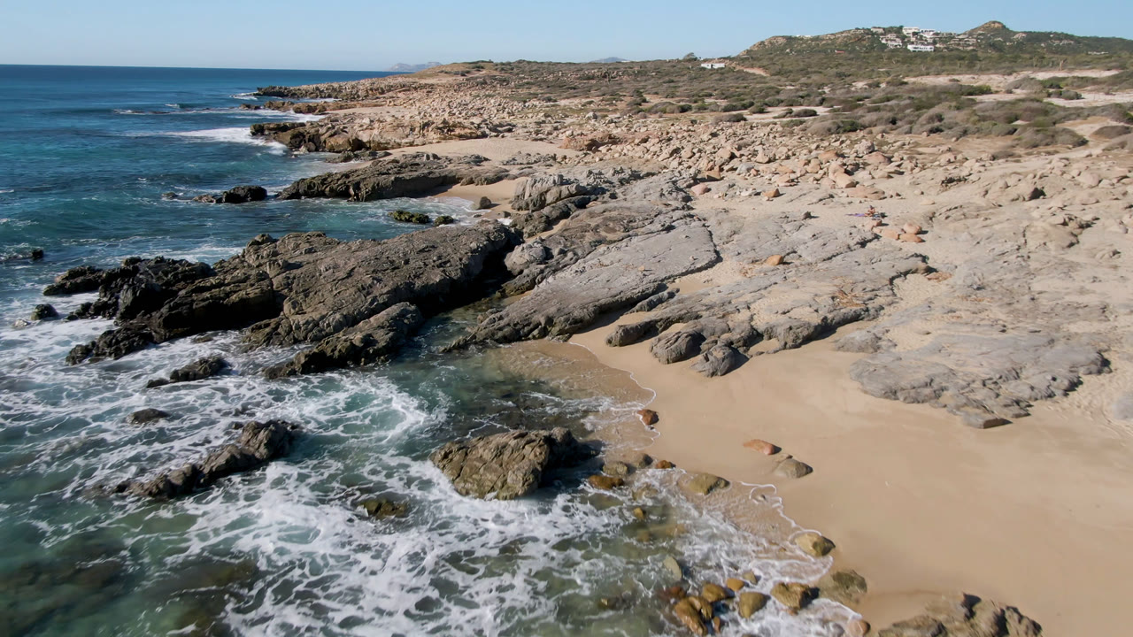 Elevated view of rocky beach, surf, sand cove, and open ocean.