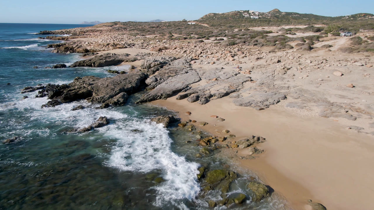 Rocky shoreline and sandy beach with ocean foam below.