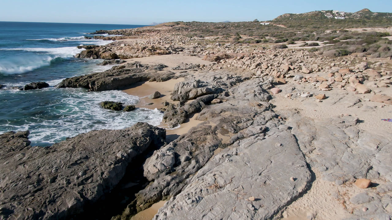 White surf breaks along rocks on a dry coastal beach