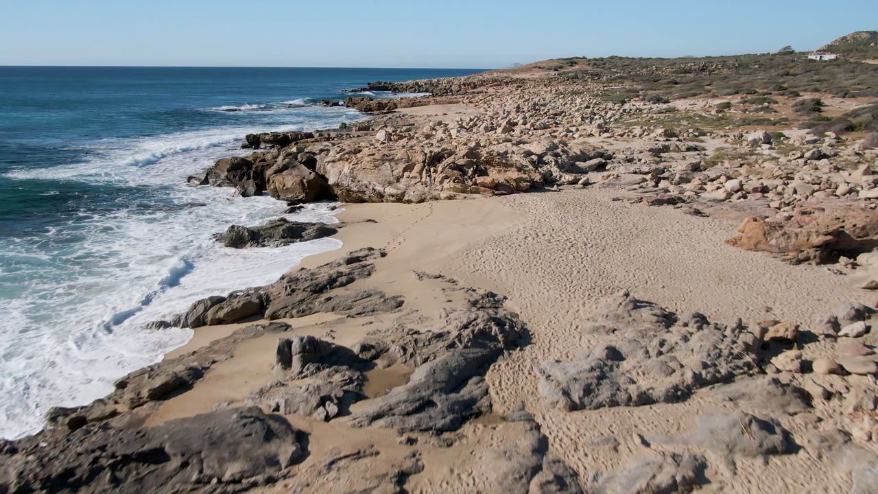Foamy wave spreads along a sandy beach beside rocky outcrops.