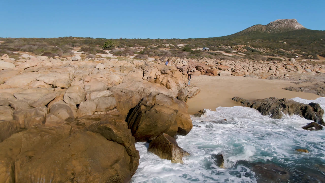 Ocean foam breaking against large tan rocks beside a sandy beach.