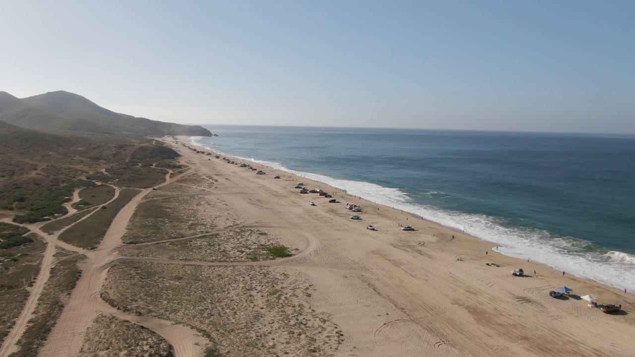 Drone frame of beach access tracks, sandy coast, surf, and blue water.