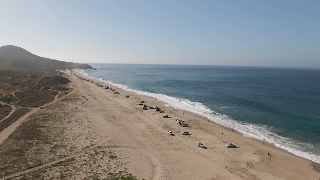 Long sandy coastline with vehicles parked near the waves