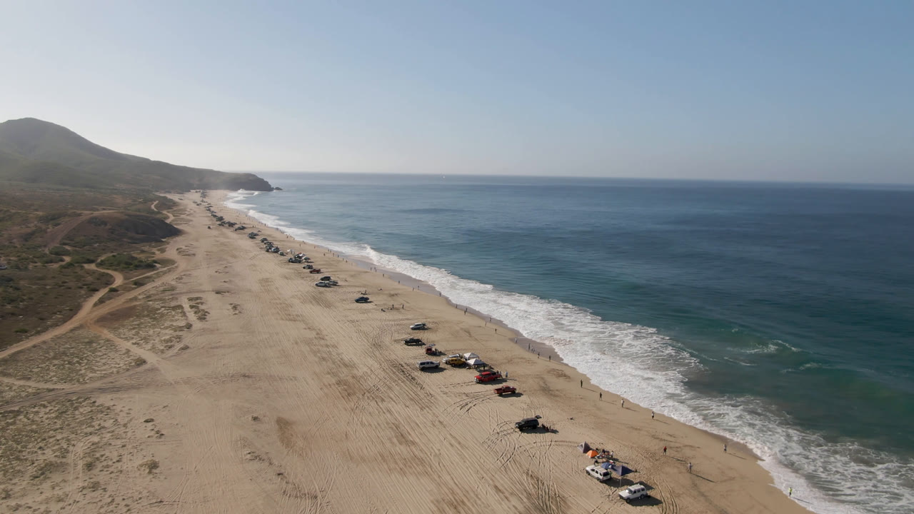 Vehicles parked on a sandy shore beside blue ocean