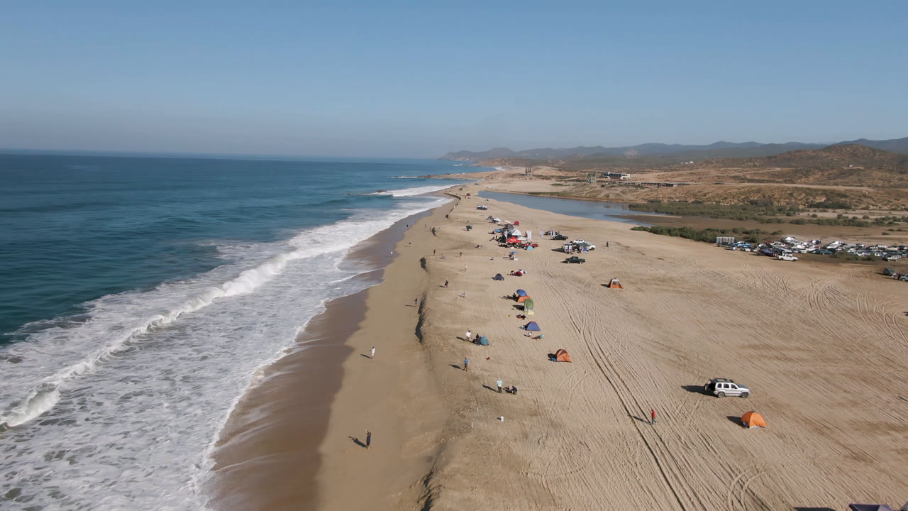 High coastal view of surf, open sand, beach umbrellas, and inland hills