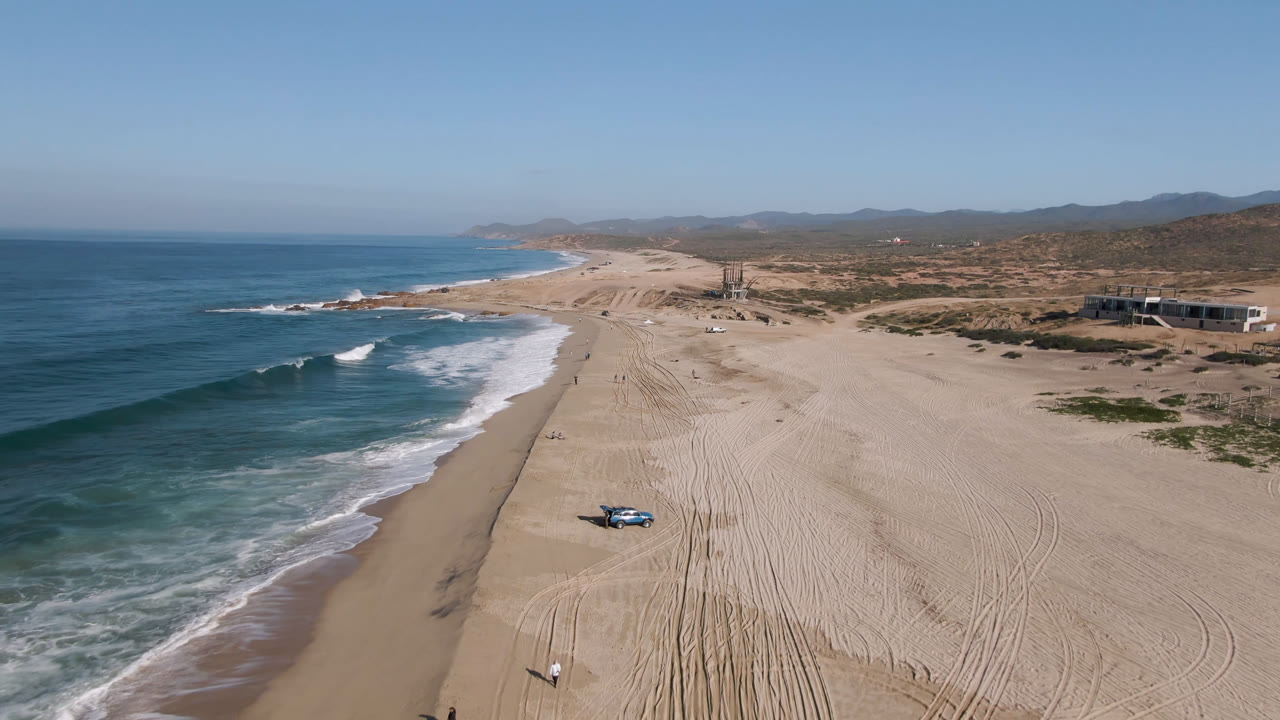 Blue truck on empty beach with waves and sand tracks