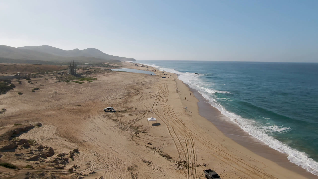 Truck and tire tracks on open beach beside blue ocean.