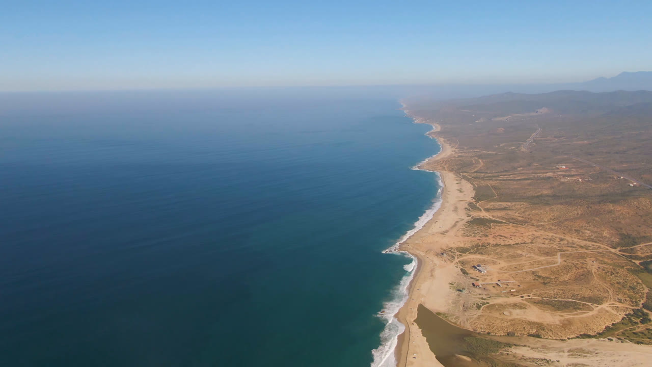 Drone view of surf, beach, and inland desert terrain.