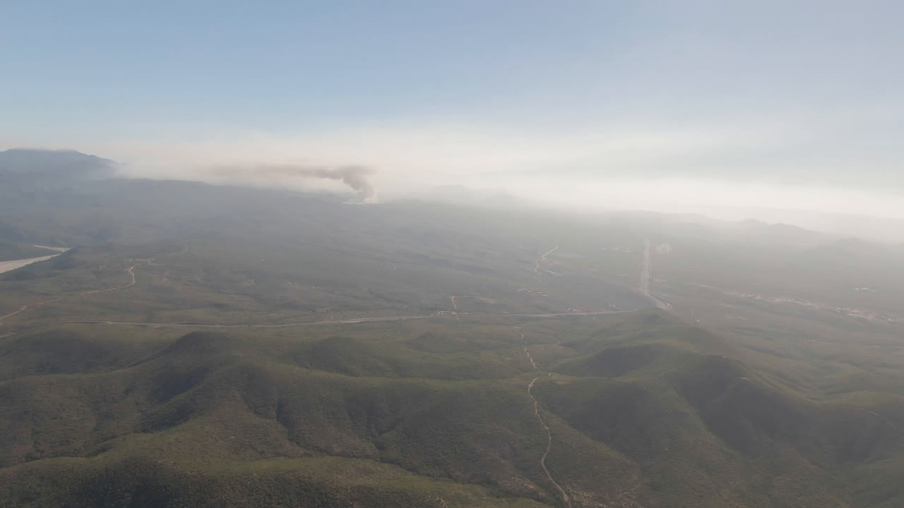 Aerial view of hazy hills with a road and distant smoke