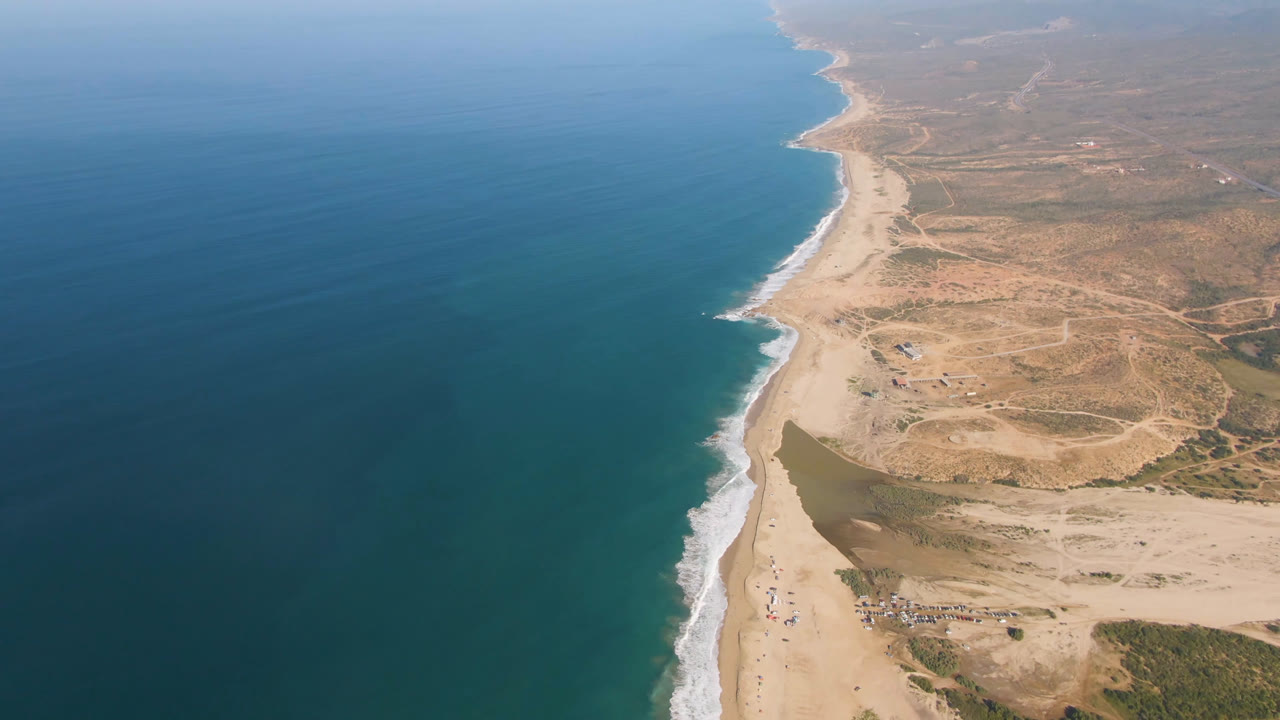 Oblique aerial view of coastline with surf, sand, lagoon, and inland desert