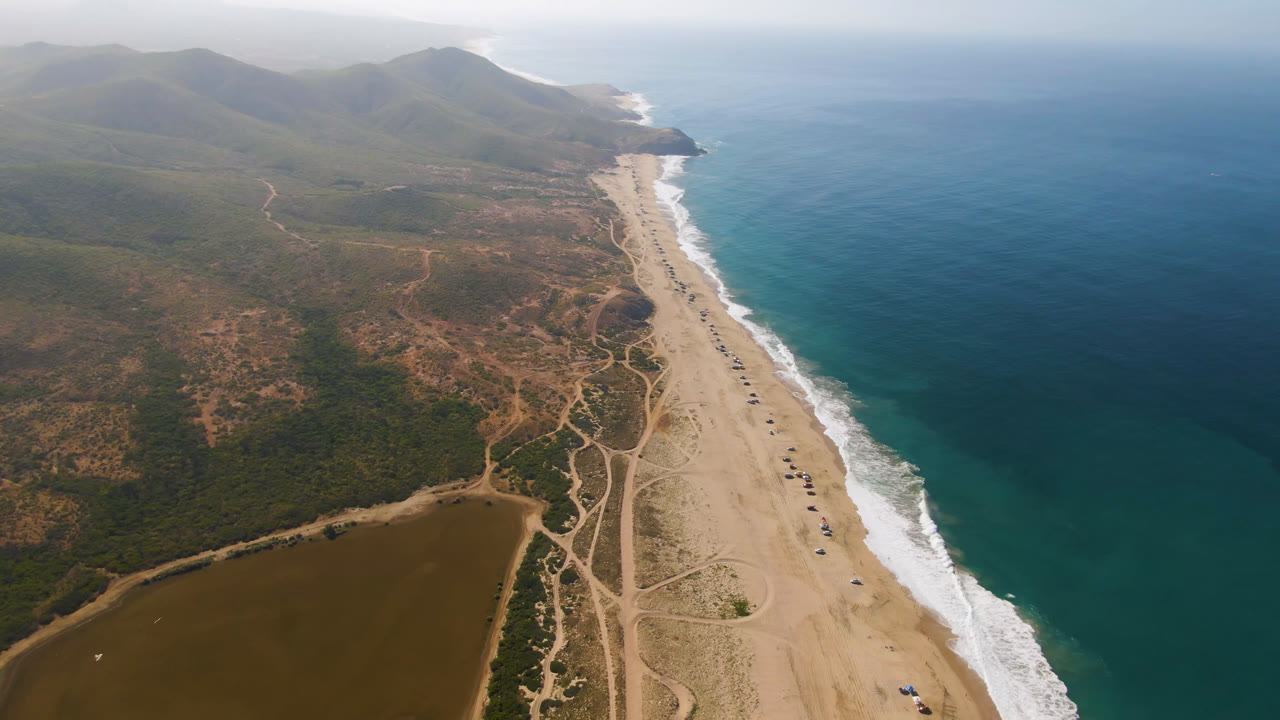 Aerial view of sandy beach, ocean, scrubland, brown water, and mountains