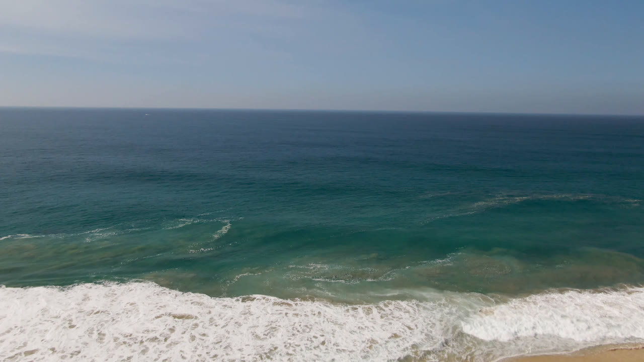 Blue-green ocean and white surf near the beach with a clear horizon.