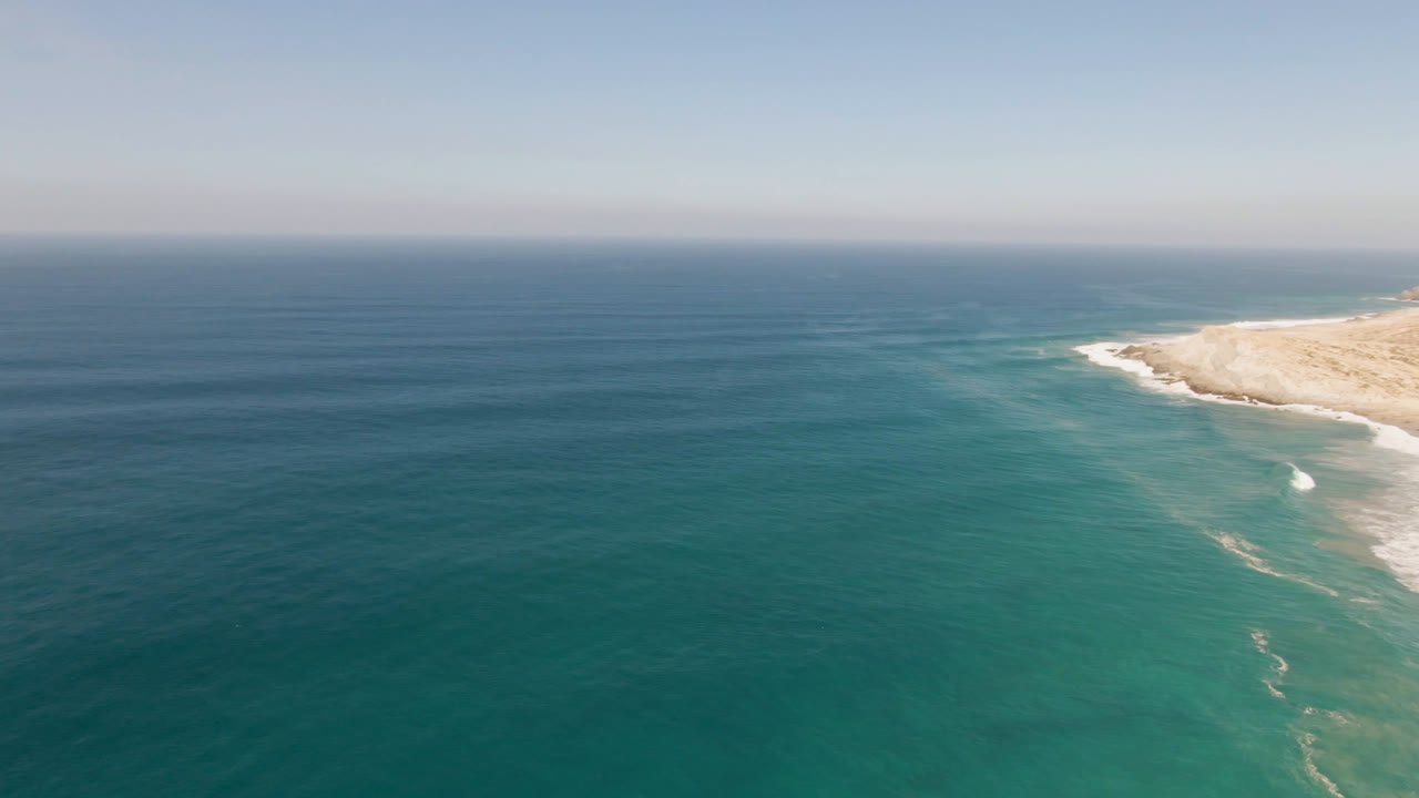 Ocean horizon above turquoise water and a pale sandy cliff at the upper right.