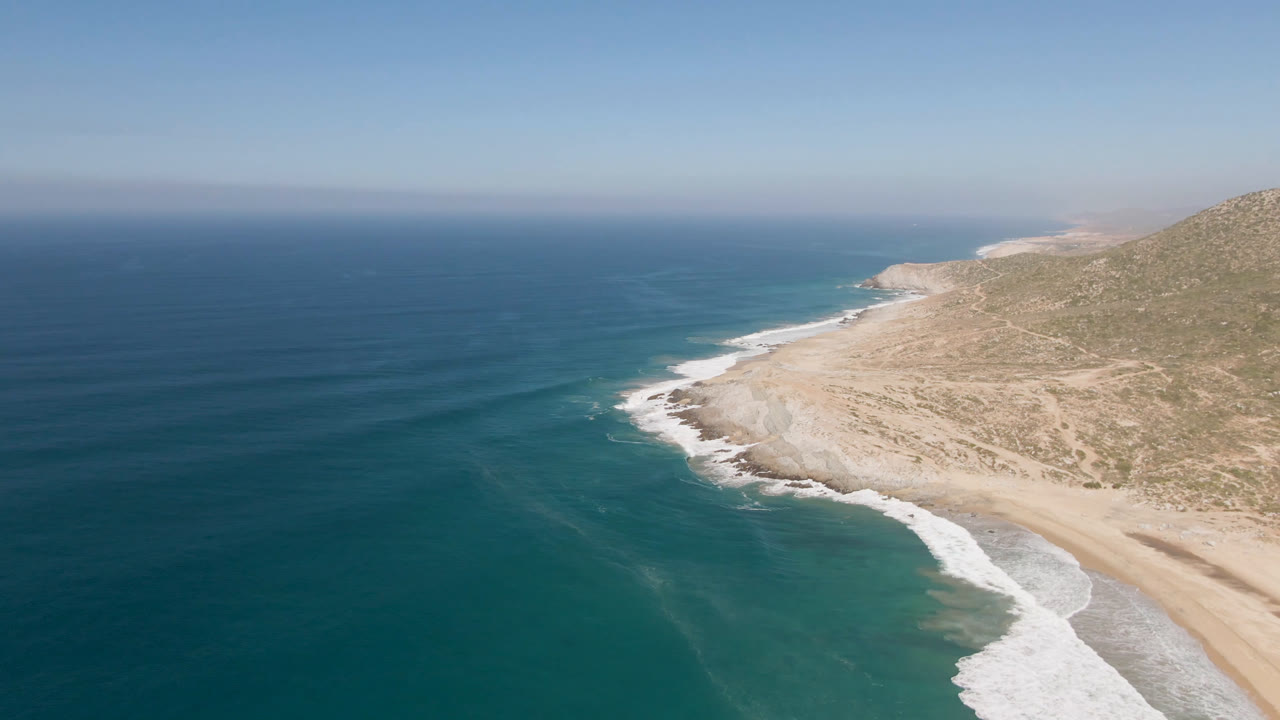 Ocean and rocky beach edge seen from above with dry coastal slope to the right.