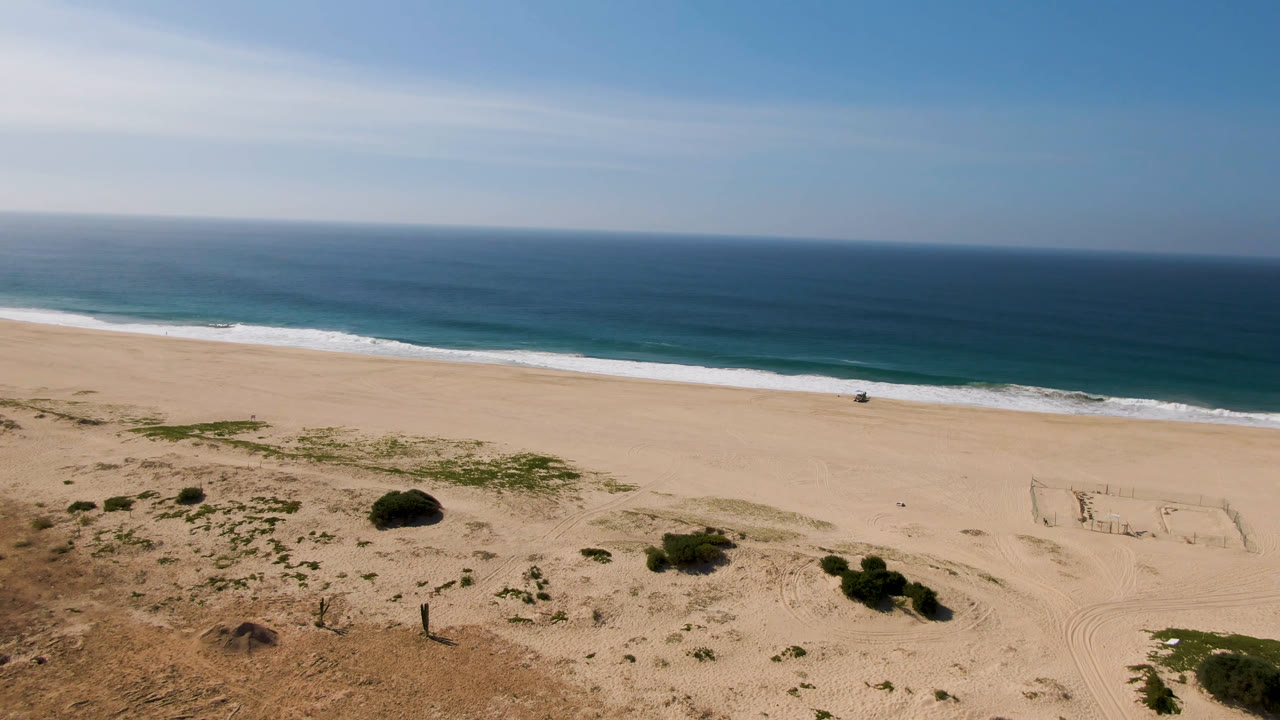 Elevated beach view with sand soccer field, surf, ocean, and sky.