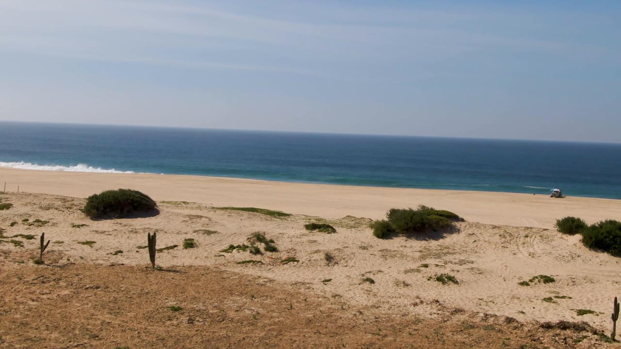 Opening frame of Migrino, Baja California Sur, Mexico with dry scrub and upright cactus-like posts in the foreground, pale beach and blue ocean beyond, and no visible people.