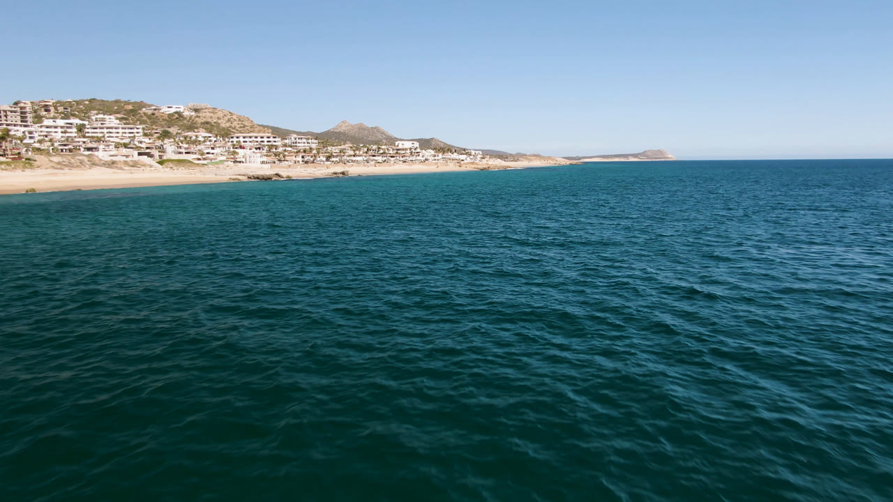 Open sea with coastal buildings on a hillside and rocky landforms beyond.