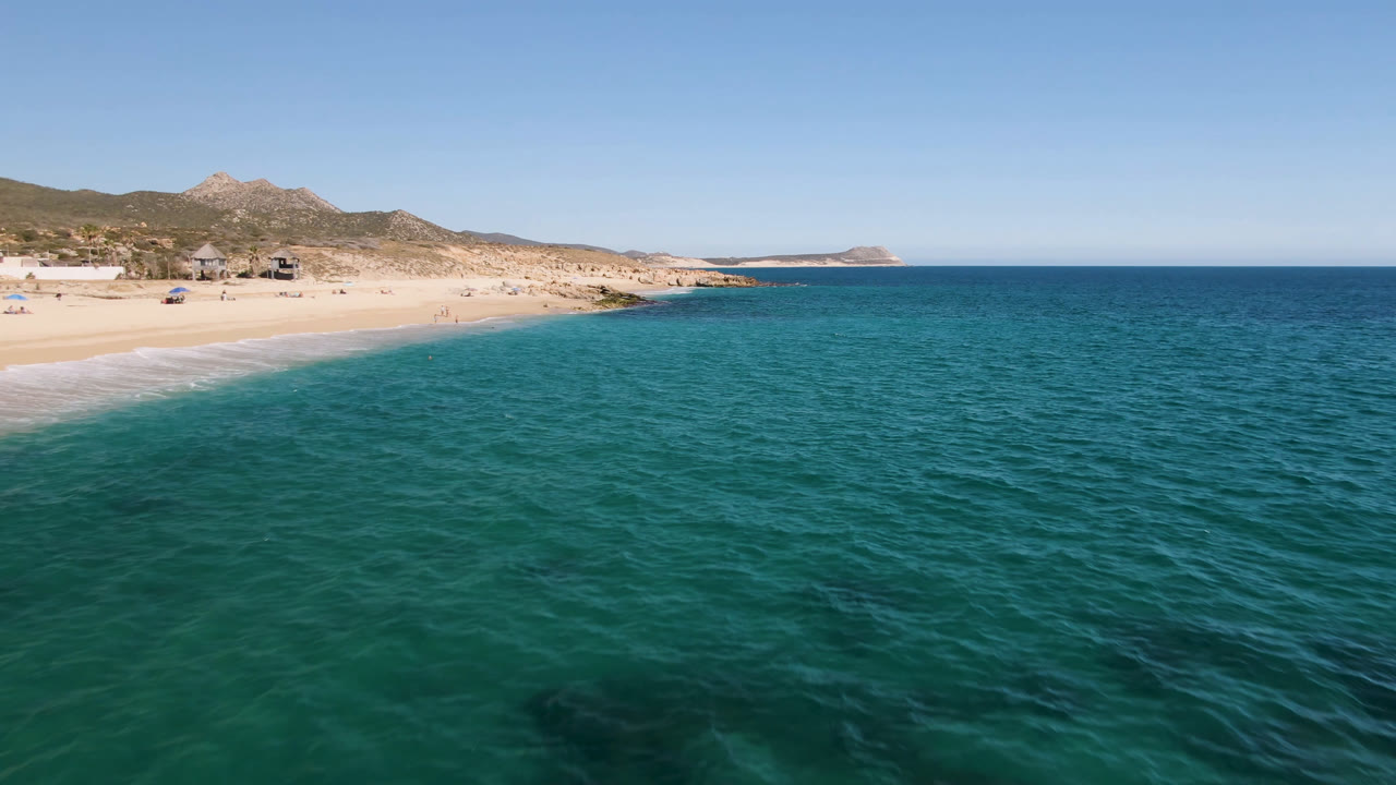 Wide aerial coastal view with ocean, beach, hills, and a clear horizon.