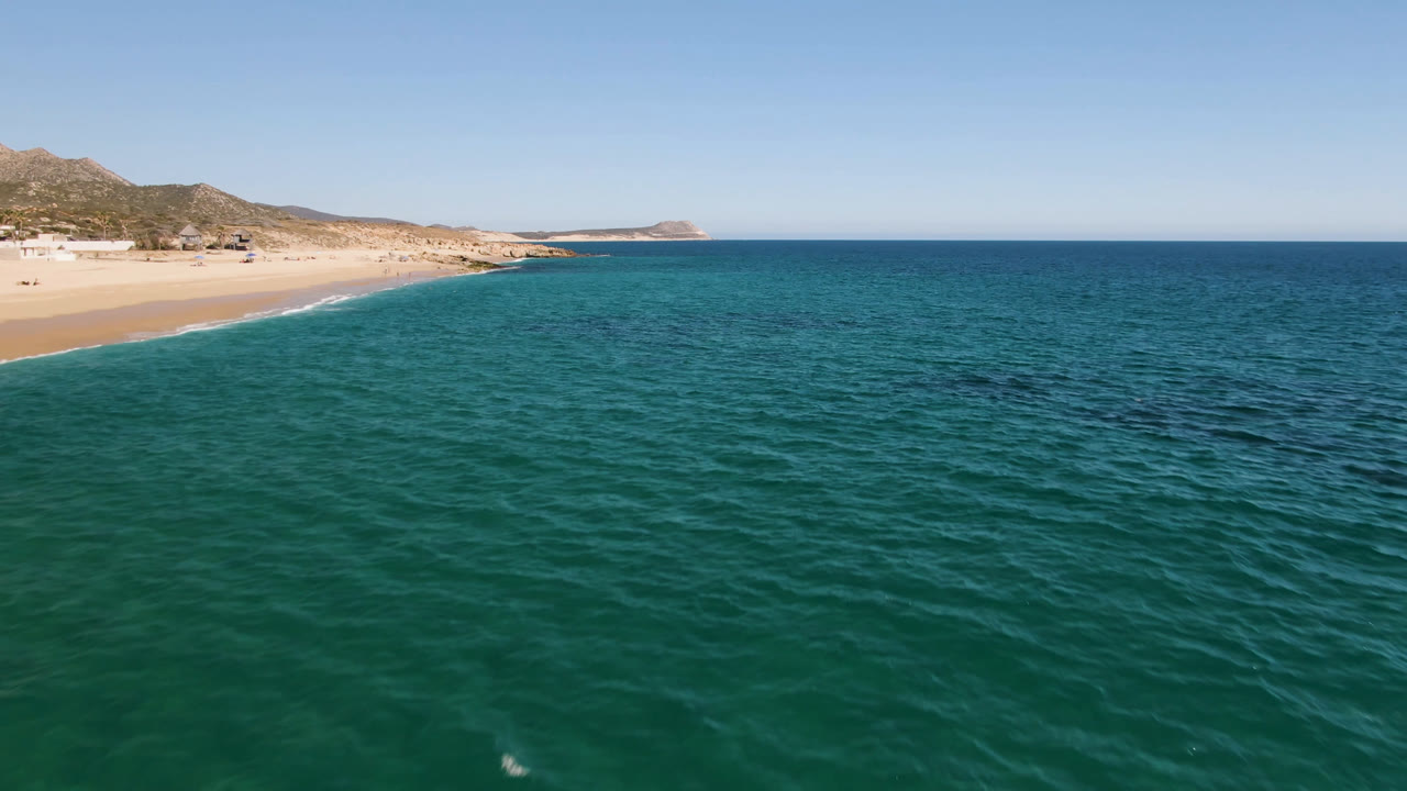 Aerial view of blue ocean beside a sandy beach and dry hills