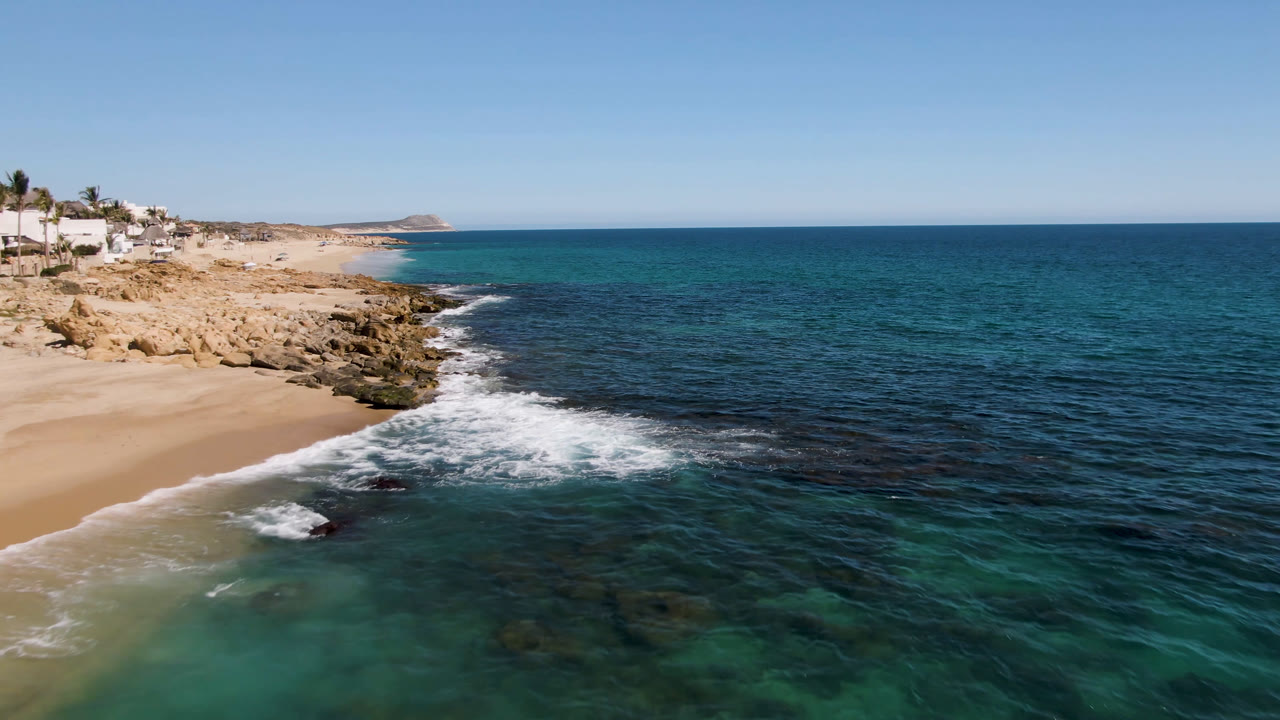 Aerial view of sandy beach, rocks, surf, and blue ocean