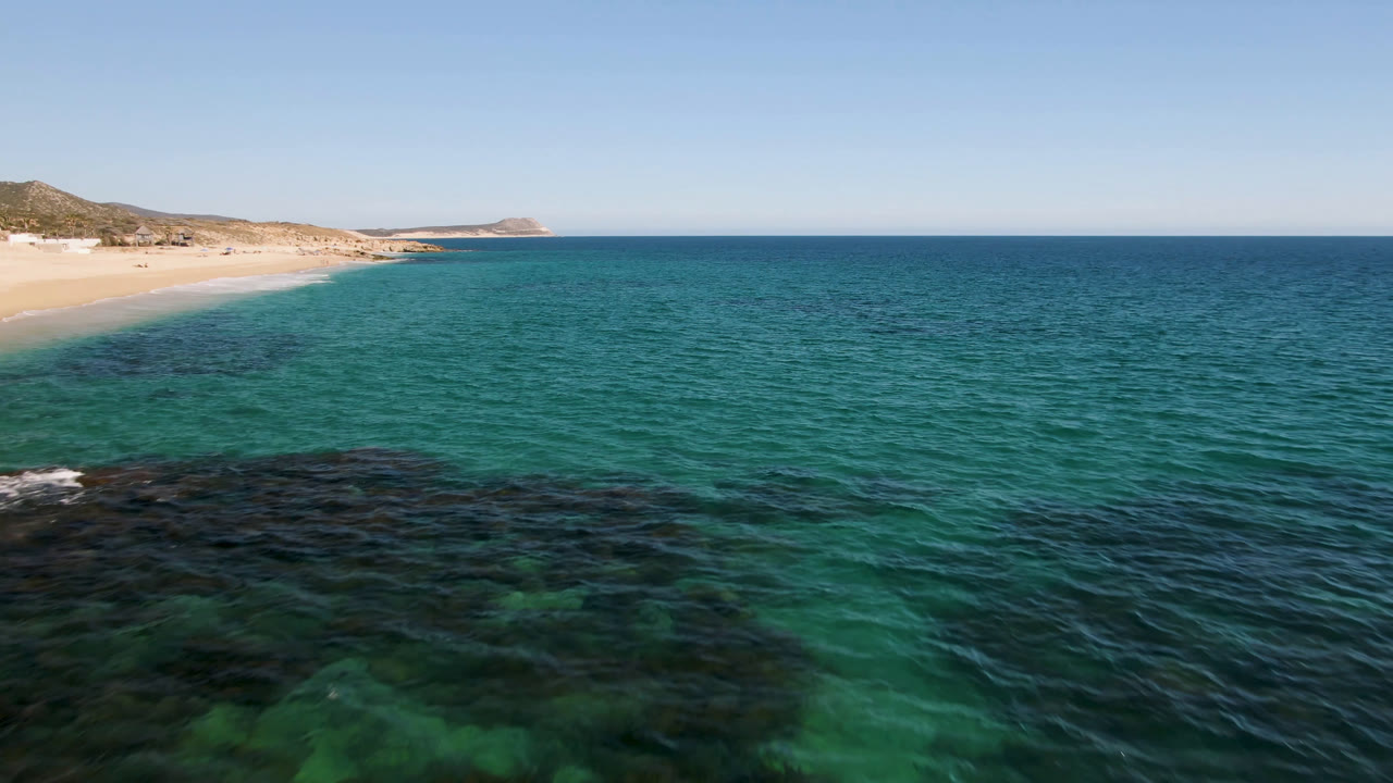 Turquoise ocean beside a sandy beach under a blue sky.