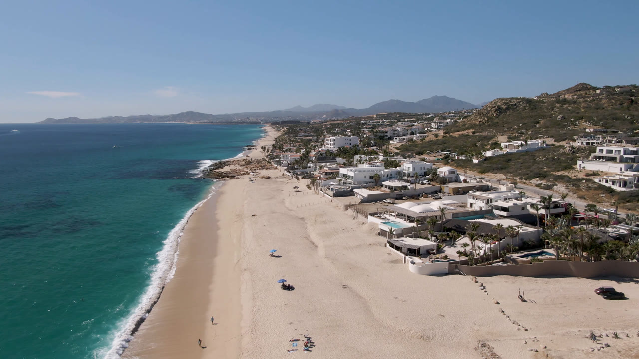 Wide aerial coastline with beach homes, hills, and blue water