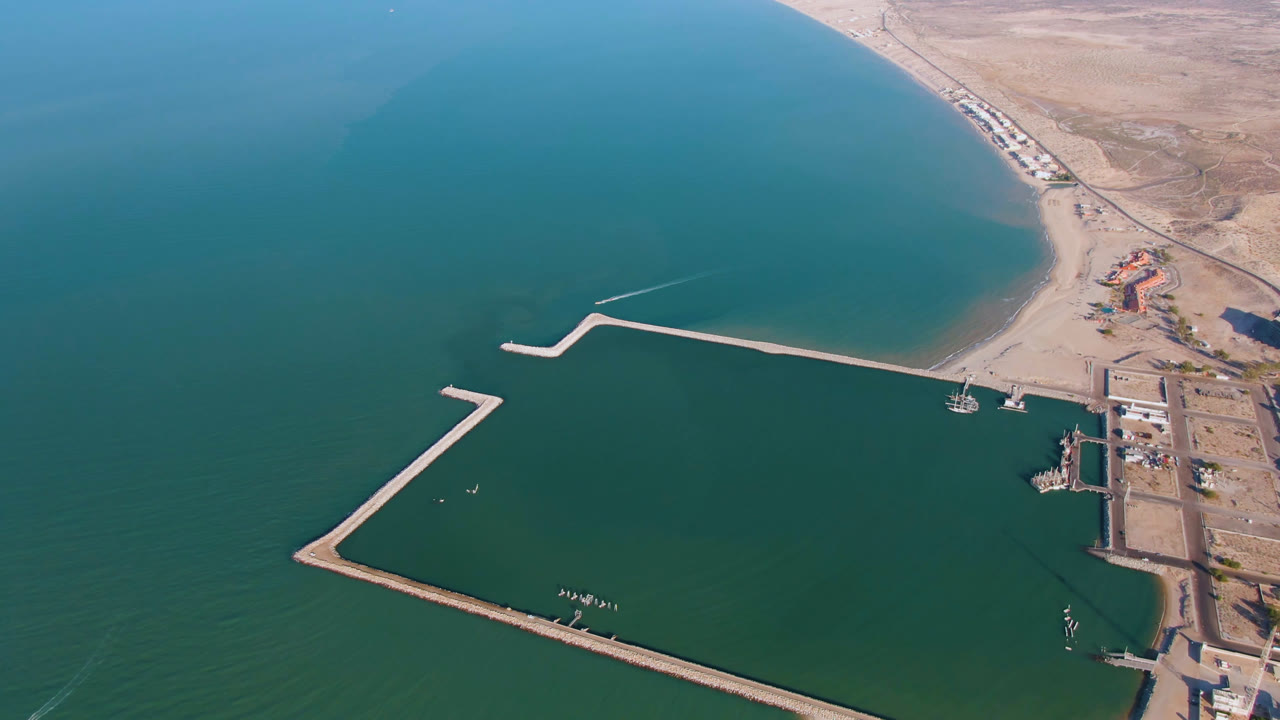 Aerial view in San Felipe, Baja California, Mexico with the long breakwater crossing the lower frame, dock structures near shore, a boat on the water, and no visible people.