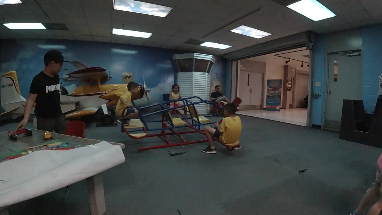 Children sit and climb on red and blue indoor play equipment.