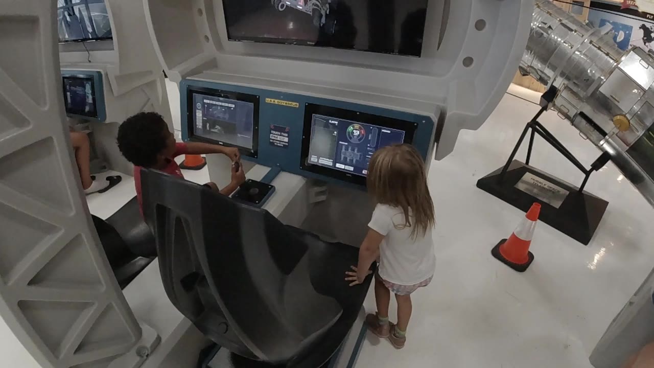 Boy reaches toward the simulator controls as girl watches.