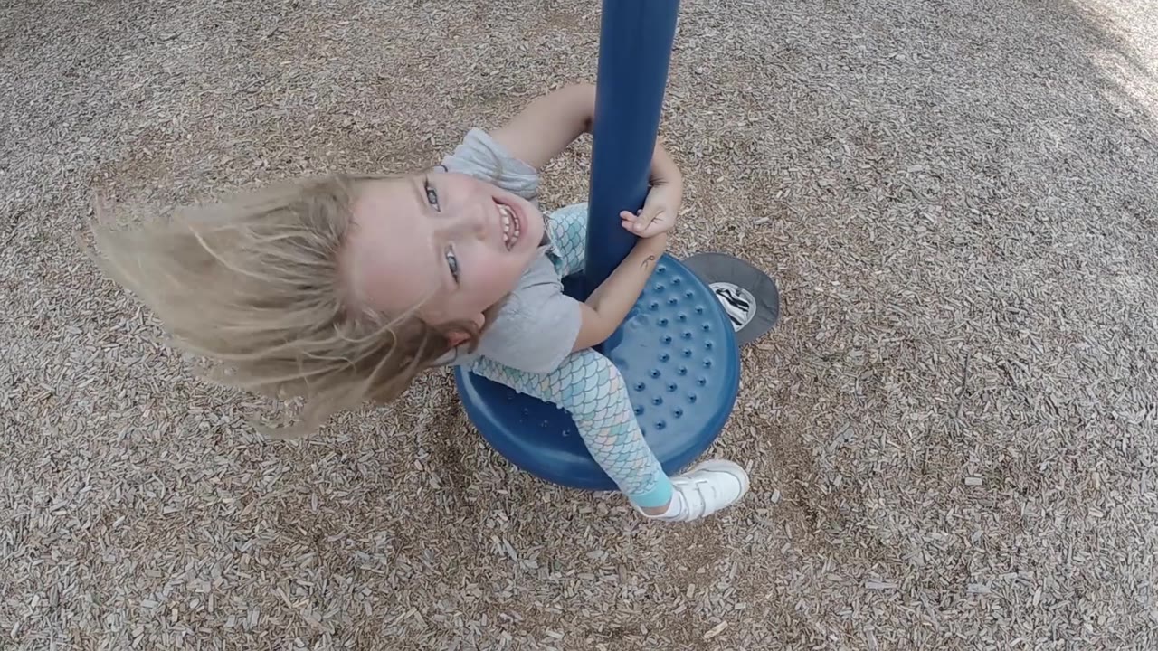 The overhead view catches the toddler rotating on the blue spinner as blonde hair sweeps out to one side.