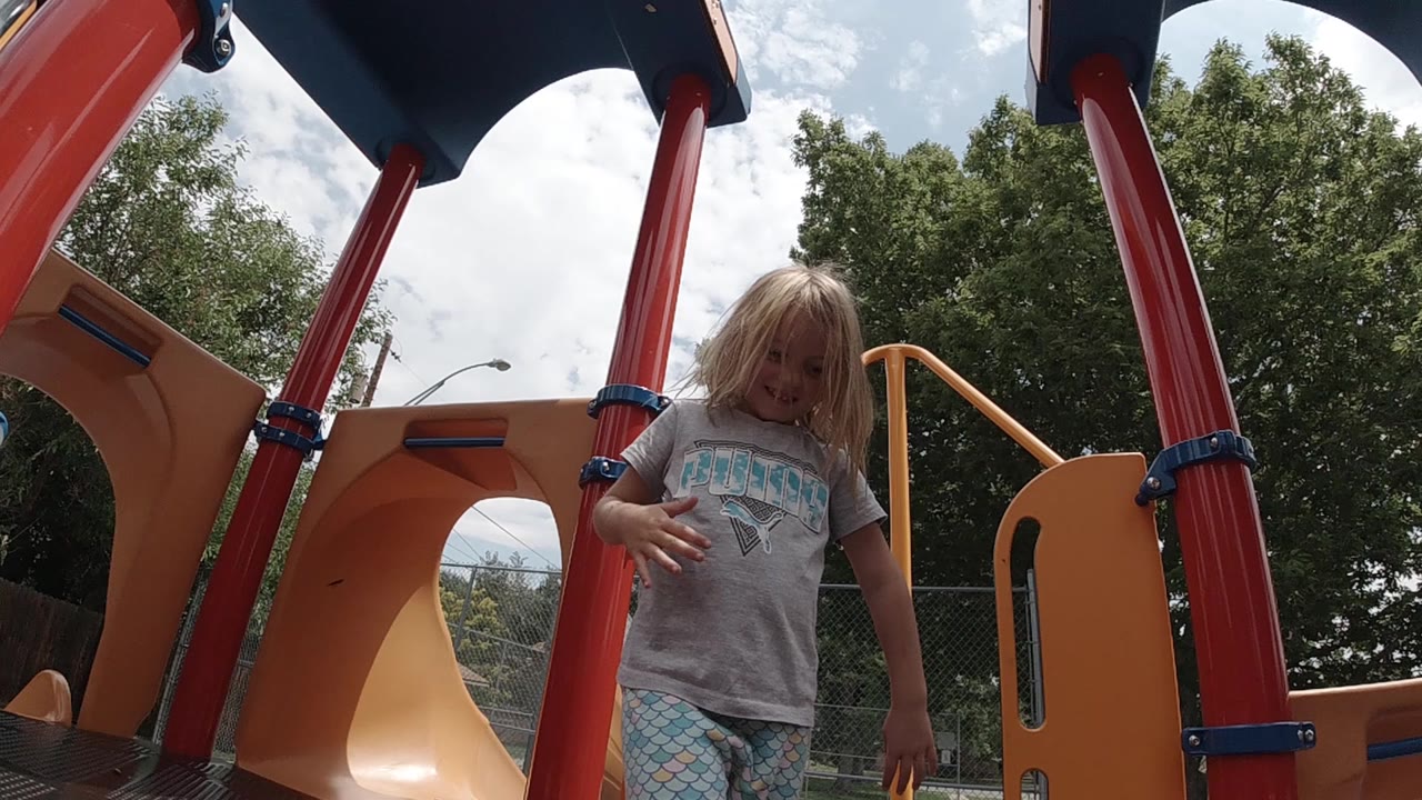 Child looks downward while standing beside red playground poles.