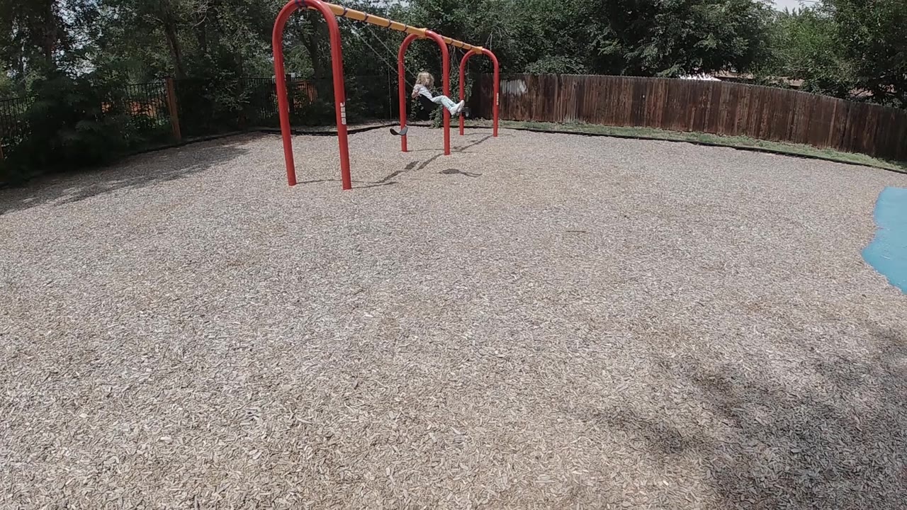 A wide playground frame shows the child near the red monkey bars, with empty gravel foreground and a blue edge visible at the right side.