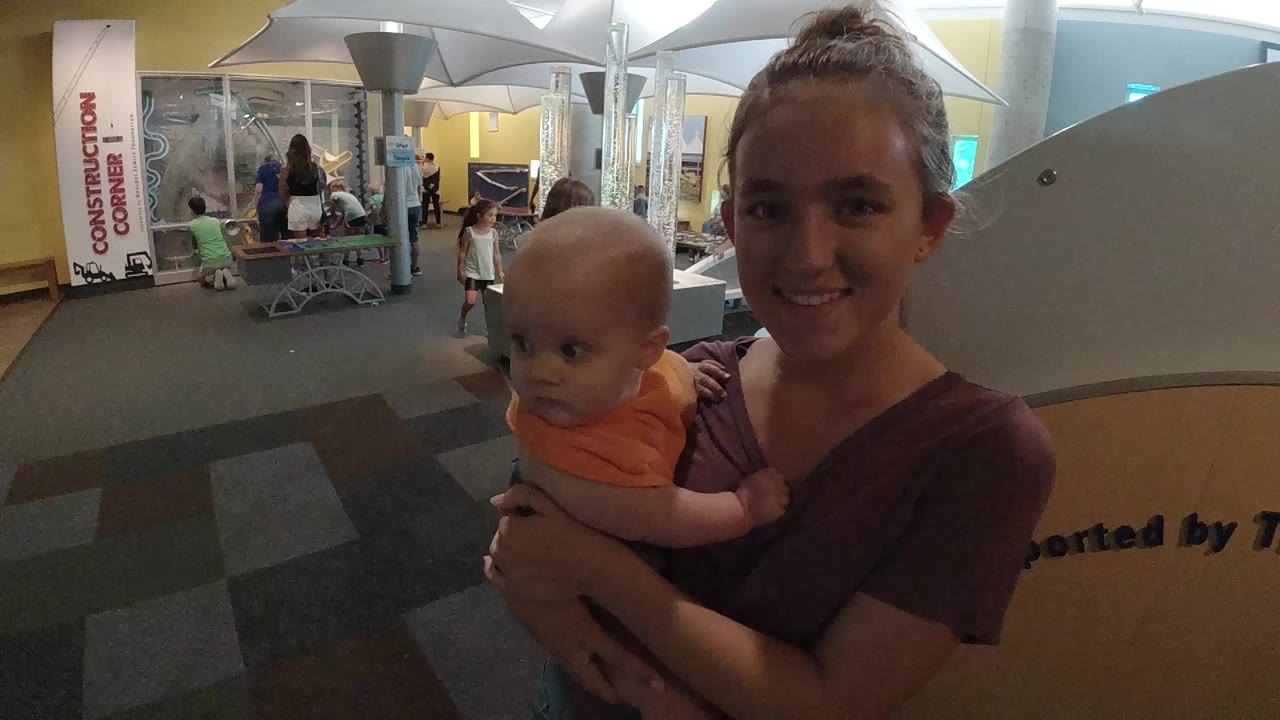 Woman smiles while holding a baby near event displays.