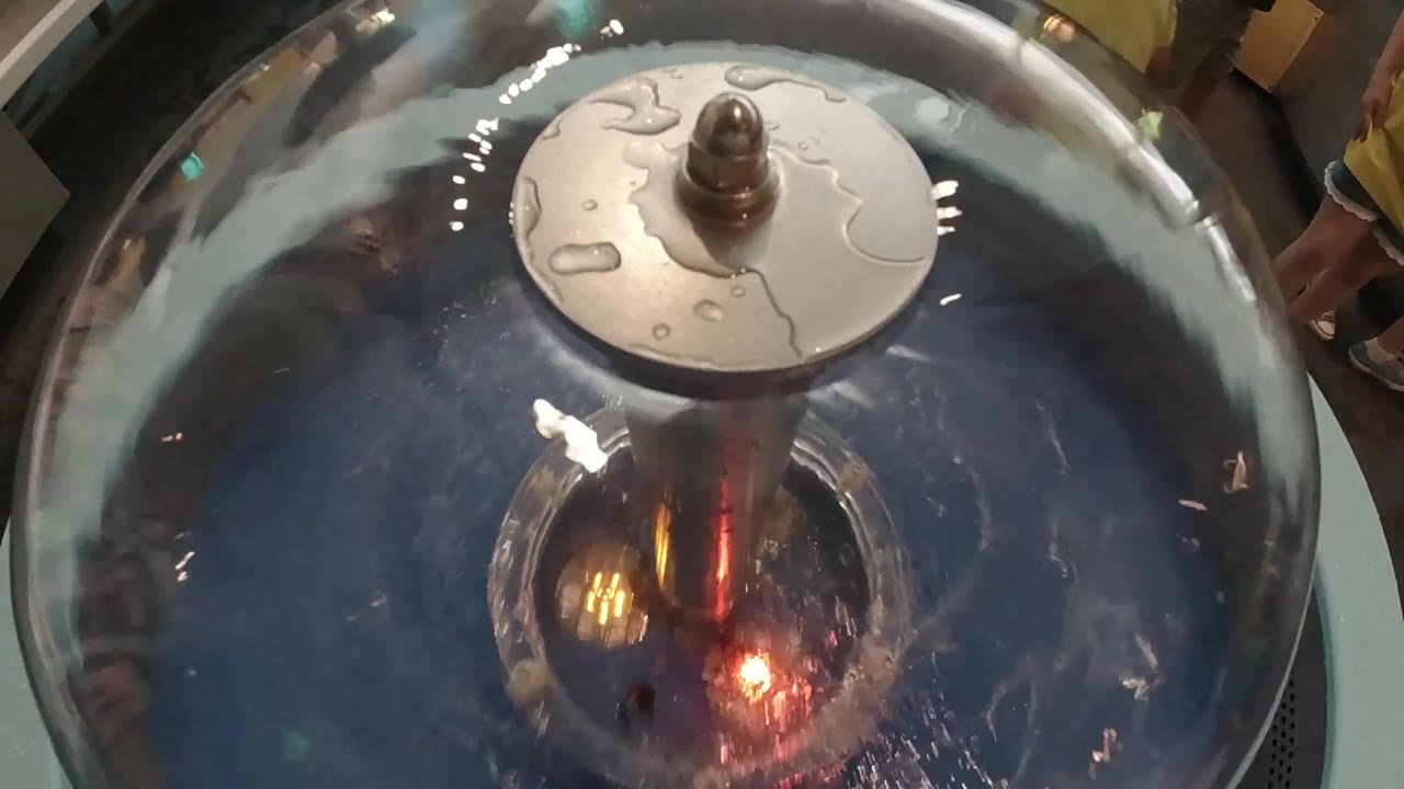 Overhead close-up of a dark steel handpan, 2019 Colorado; lighter disc element clearly centered on the dome's crown; surrounding metallic surface shows hammered tone-field texture; no visible people in frame.