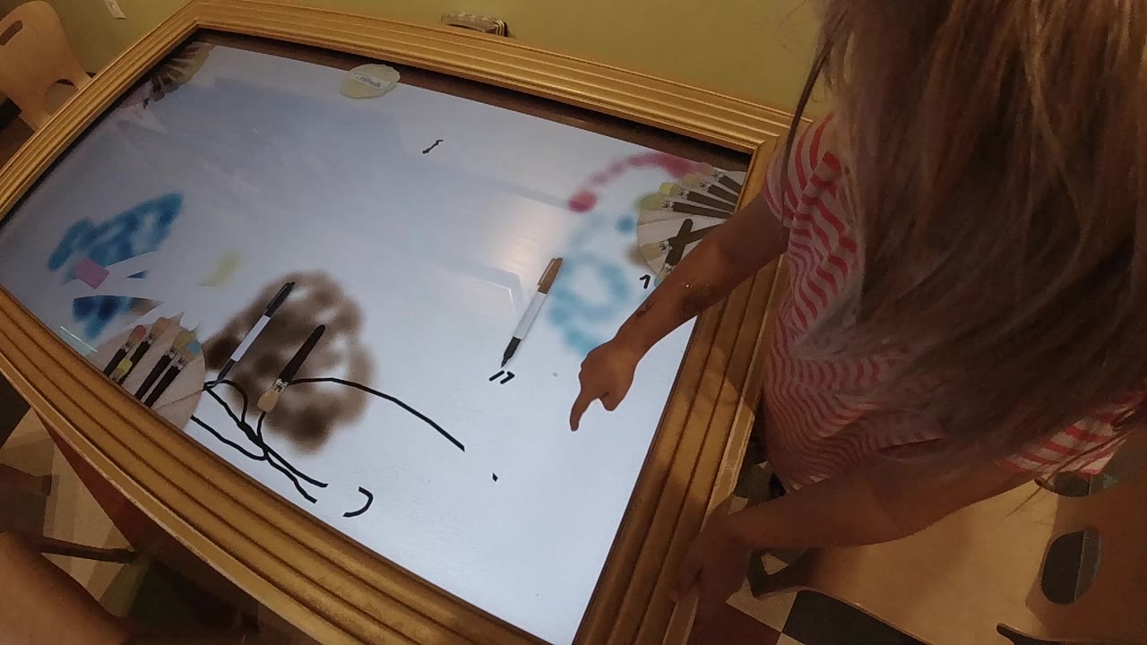 Child points toward markings on an illuminated tabletop.