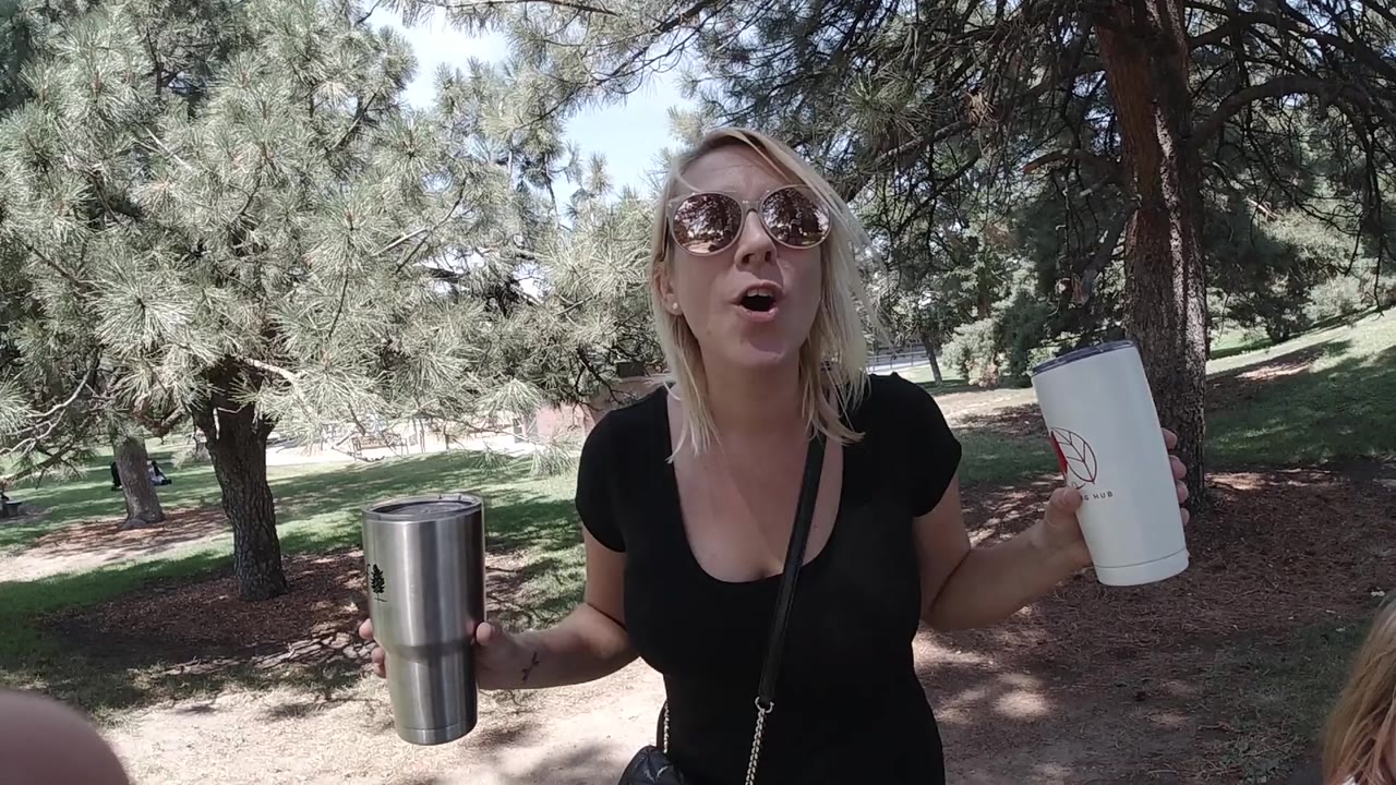 Woman in sunglasses speaking near pine trees with cups in hand