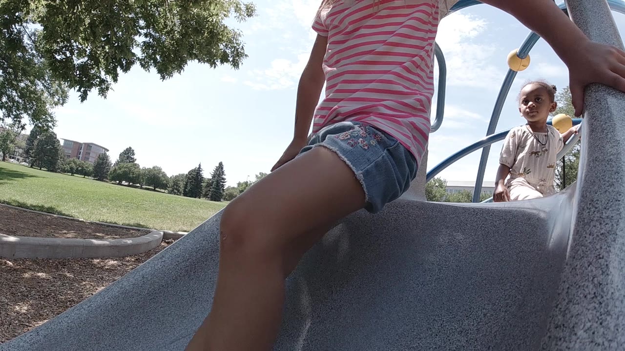 Close low view of a girl on a slide with another child behind the rail.