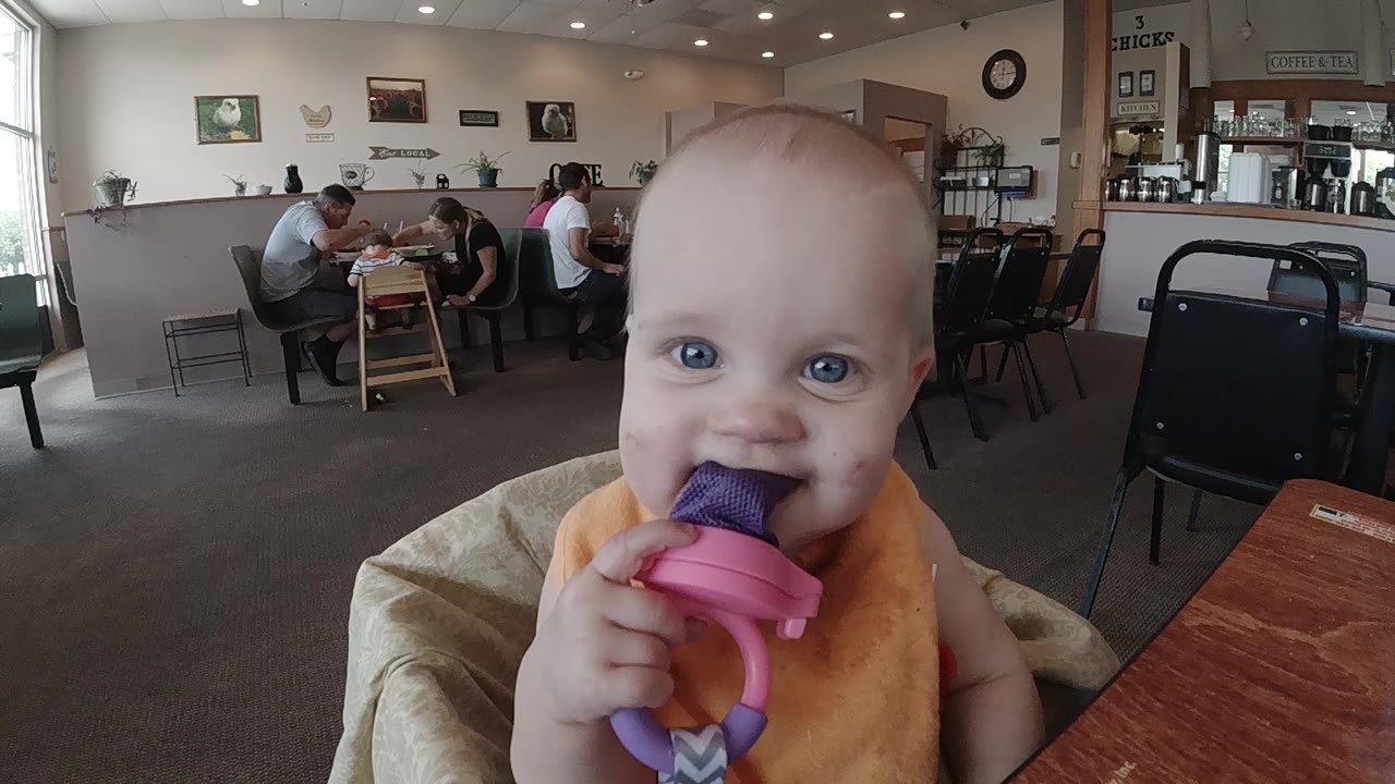 Smiling baby holds the purple ice pop near their mouth.