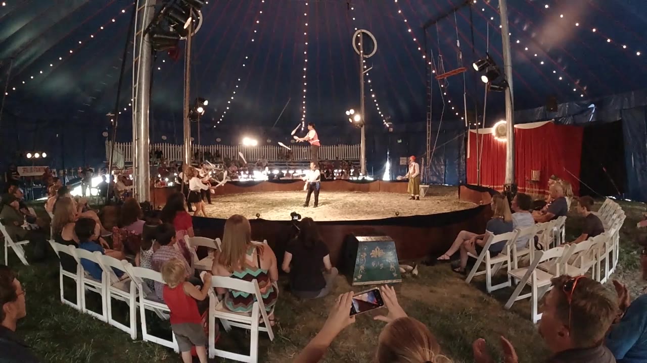 Top-down drone view of an illuminated circus ring at night with audience seating and red decorative ring border