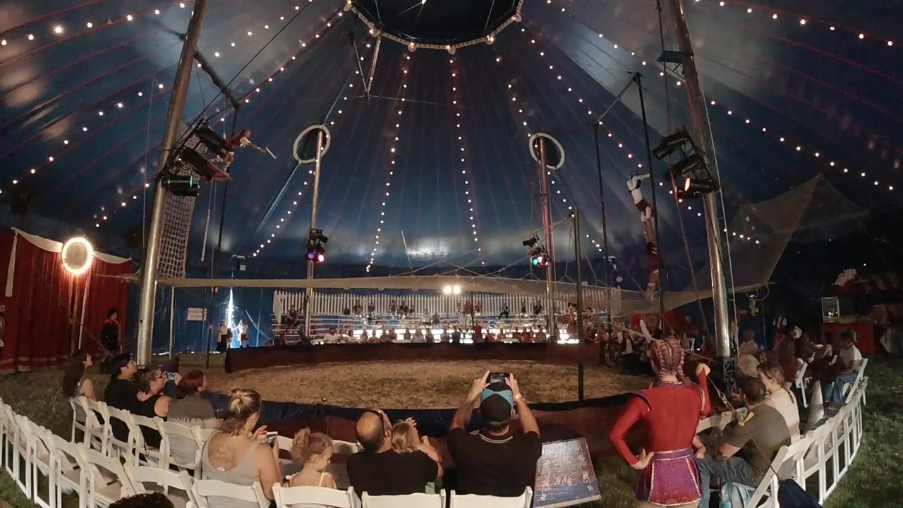 Audience watches aerial rigging inside lit circus tent