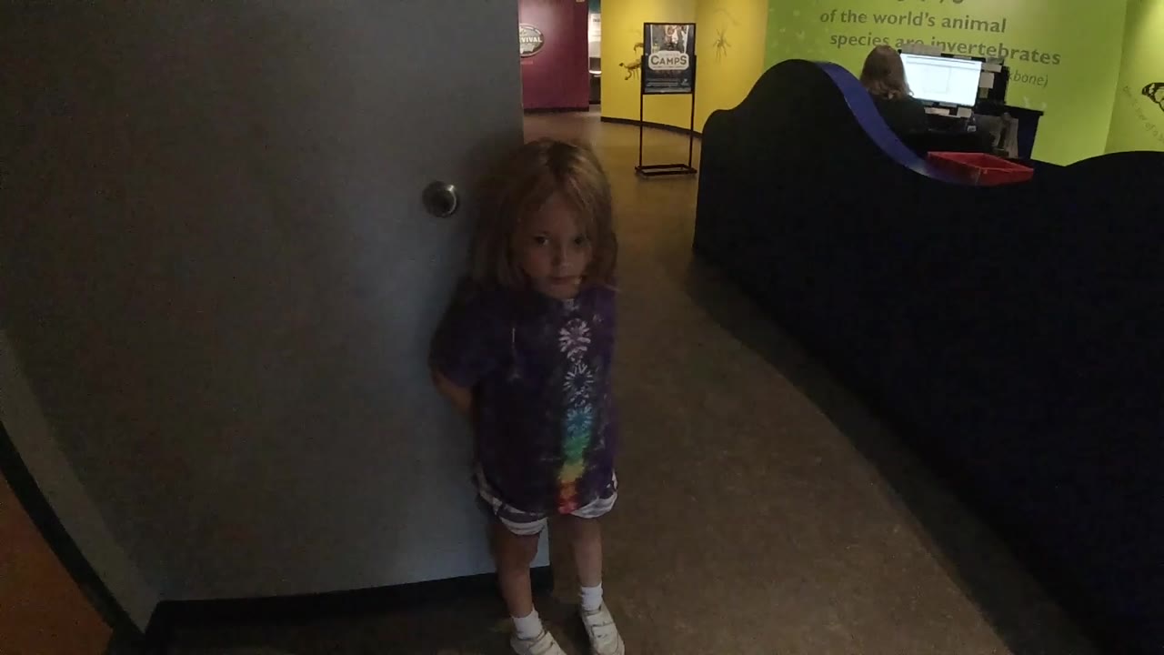 The girl stands near the door and looks forward, with the dark curved seating and bright monitor behind her in the Colorado interior.