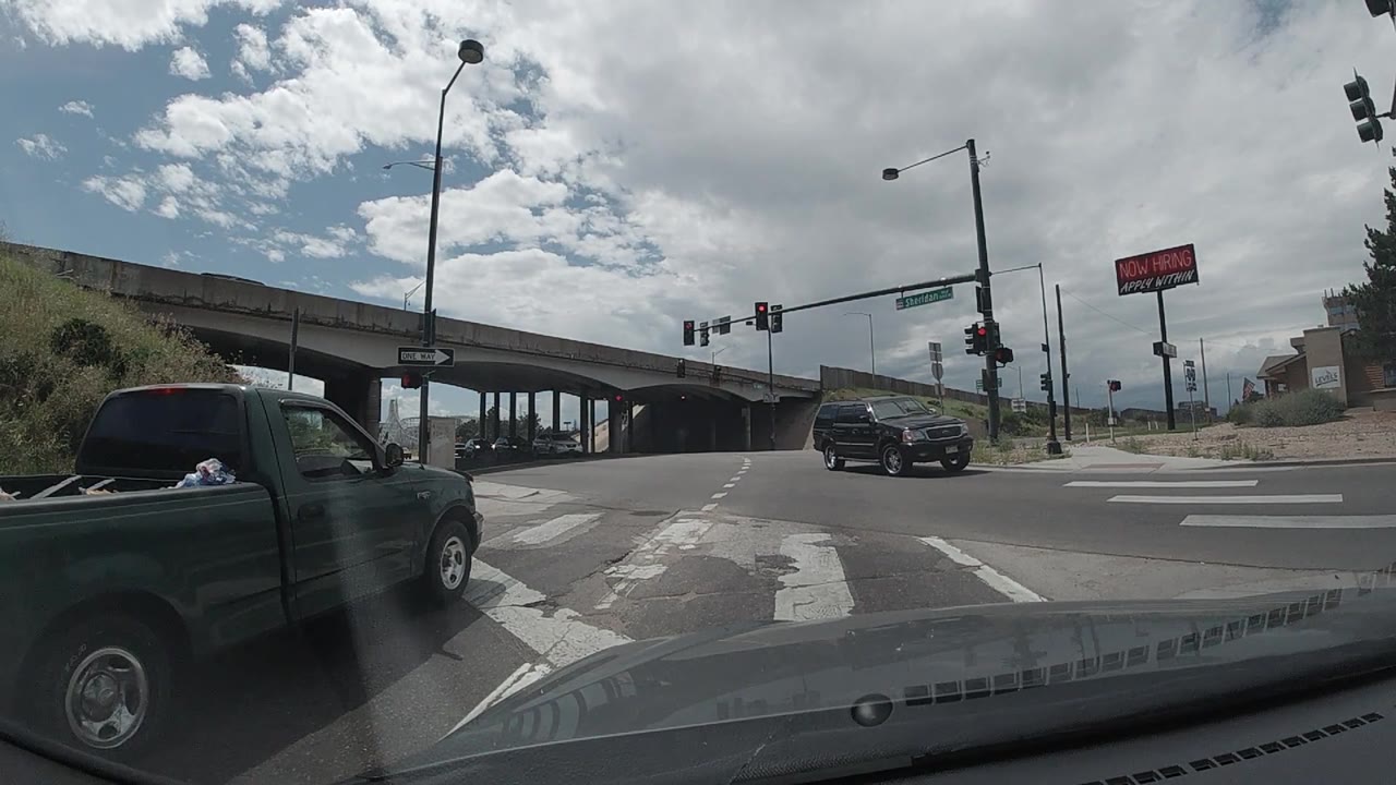 At 0:02, the black SUV is more clearly crossing the intersection from the right side toward the left, with the overpass and red traffic signals above the lanes and no visible people.