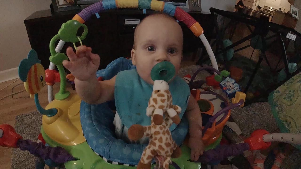 Baby looks forward with one hand lifted inside the activity center.