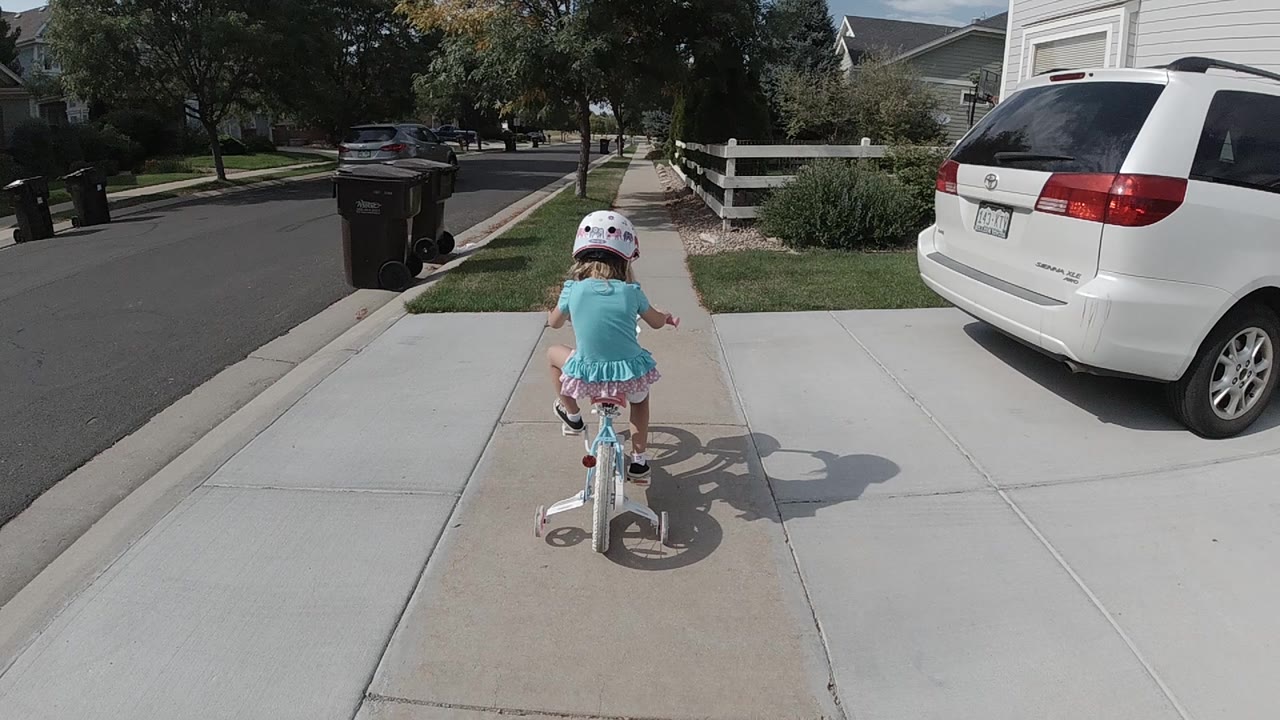 Child pedaling a bicycle down a concrete sidewalk near a street.