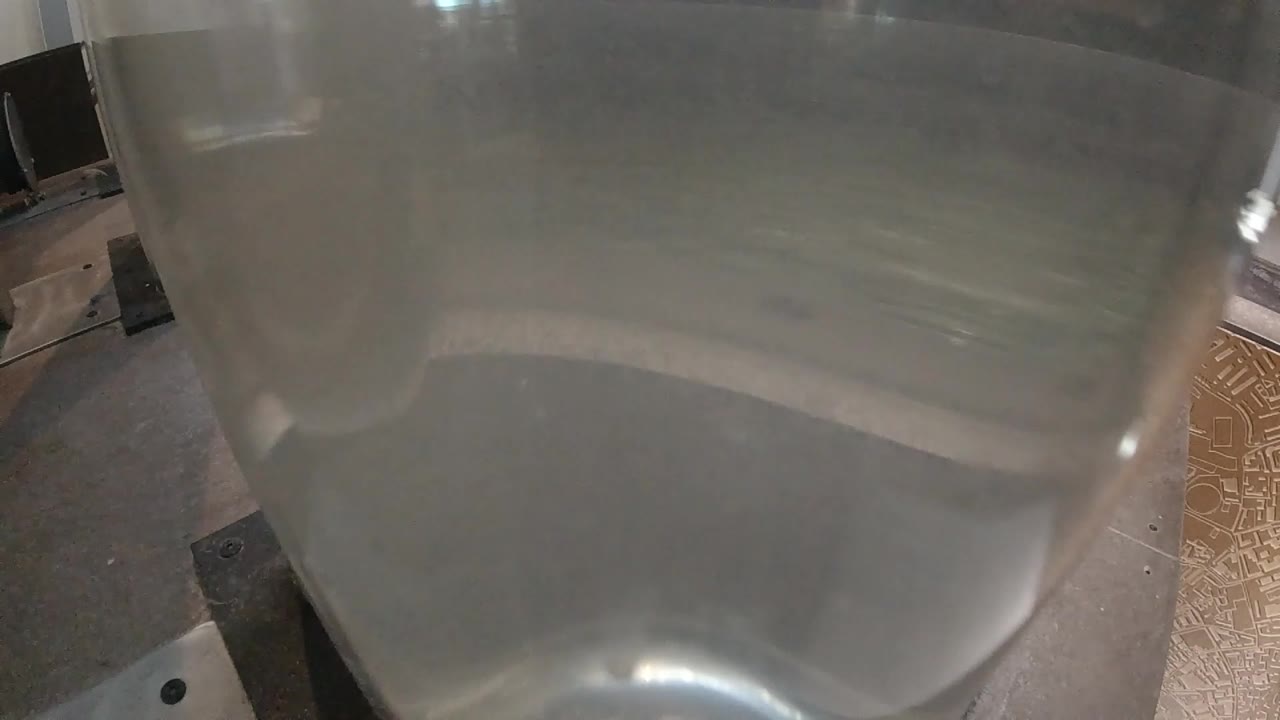 Close-up view into clear round container, water surface showing first signs of gentle movement as heat builds, container walls framing the composition, no visible people