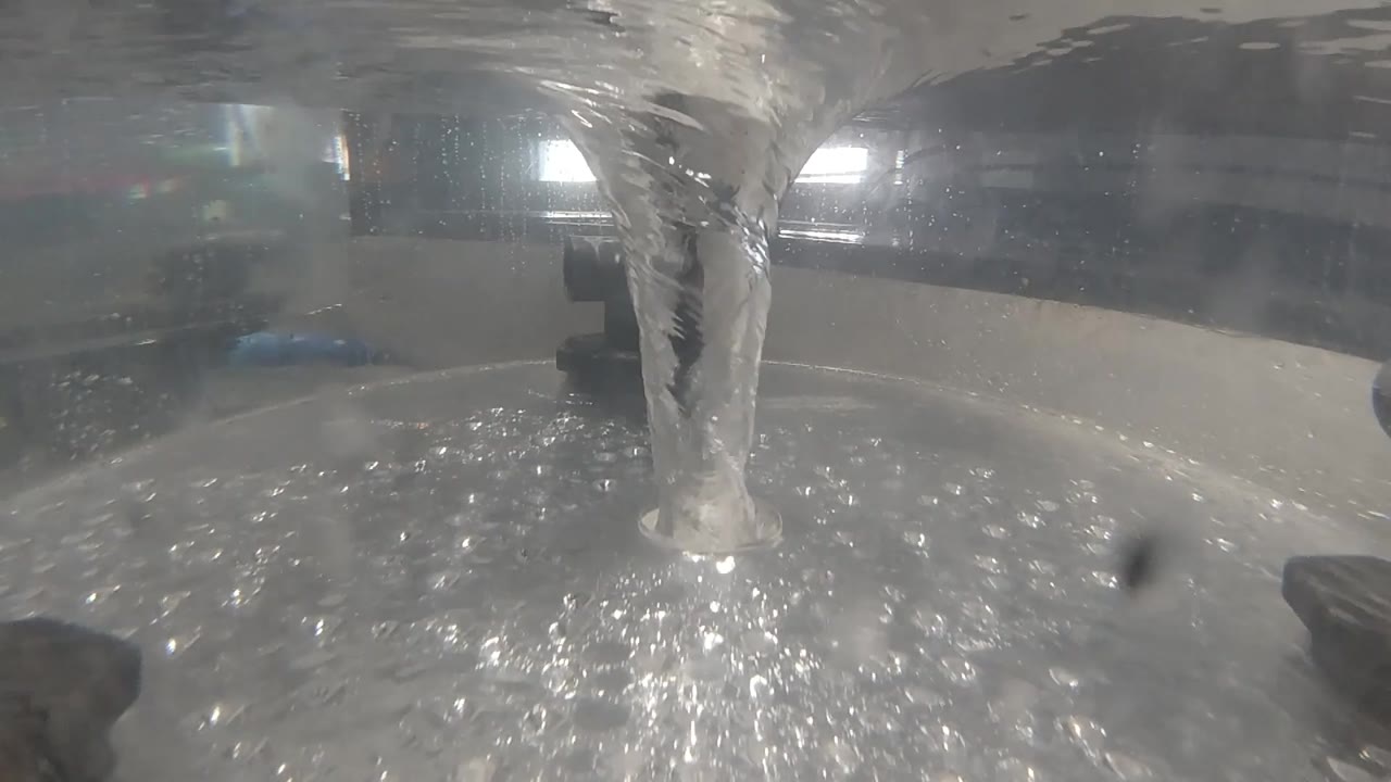 The thermal pool surface at 0:02 shows dense rippling and sparkle from the continuous pour, with two soft orbs of light glowing through steam in the upper background; Colorado; no visible people.
