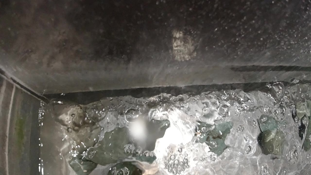 Overhead close-up of vigorously boiling water in a stainless steel pot with white foam and dark bubbles across the surface