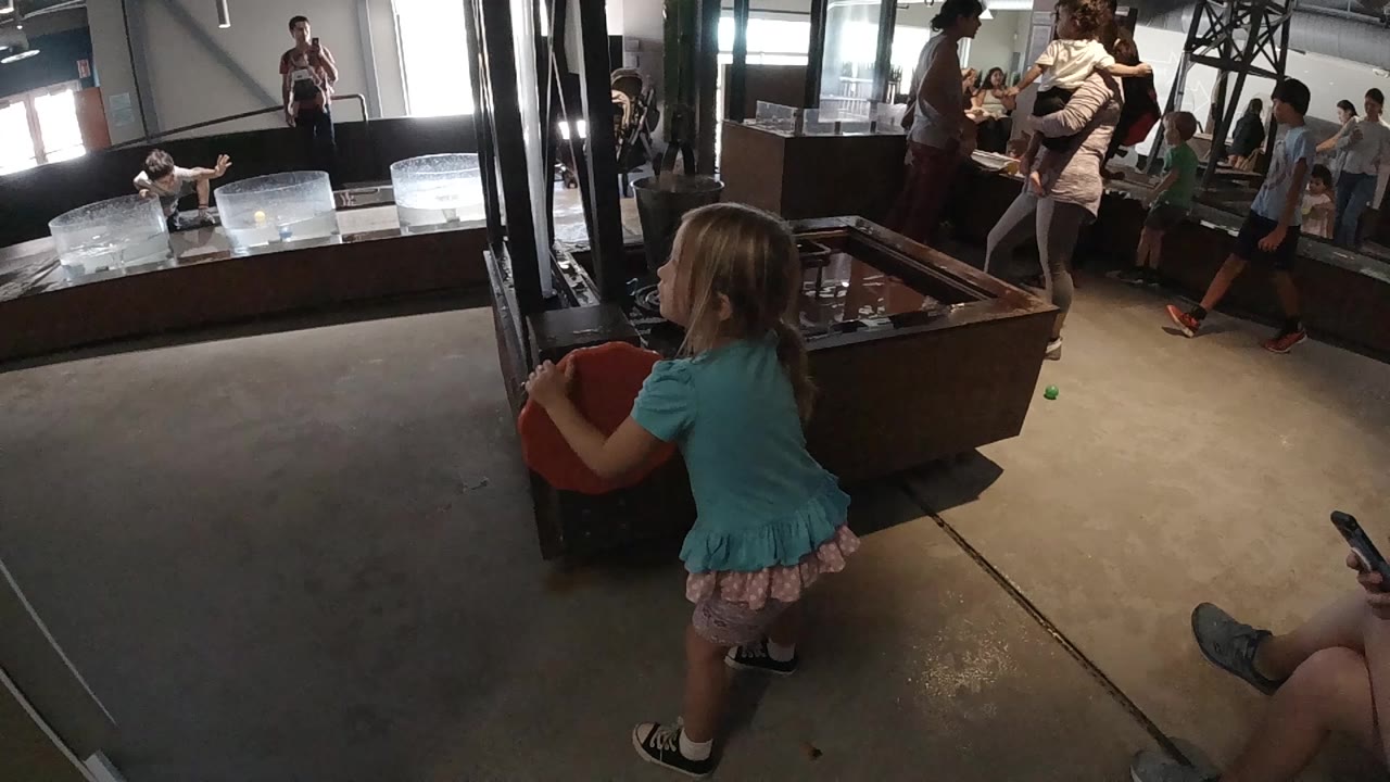 Toddler stands beside a red object with people gathered behind her.