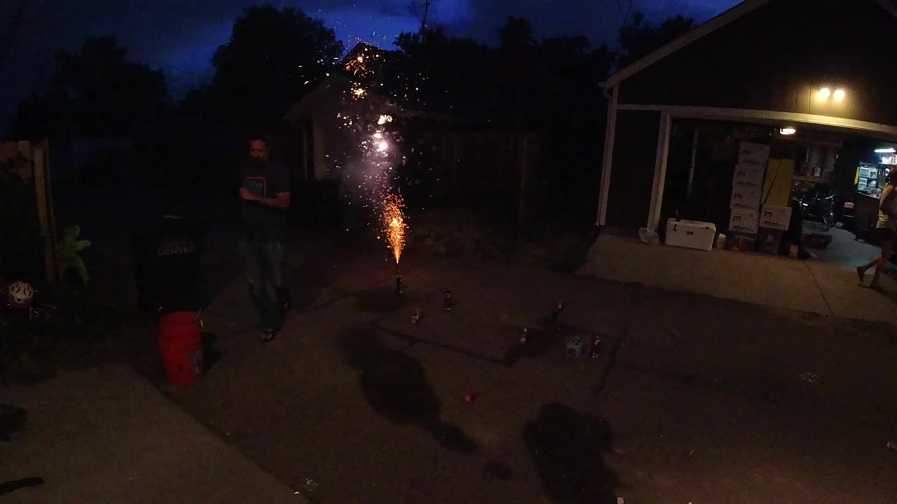 Firework fountain burns beside a dark backyard and porch.